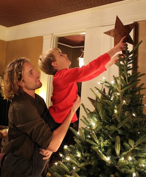 Decorating the Christmas tree, an older brother lifts his younger brother.